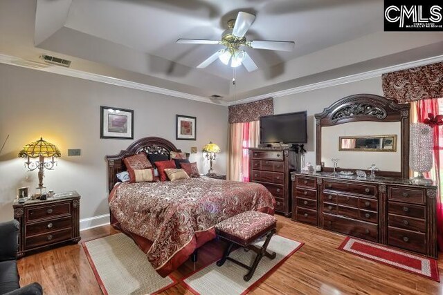 bedroom with light hardwood / wood-style flooring, ceiling fan, and a raised ceiling