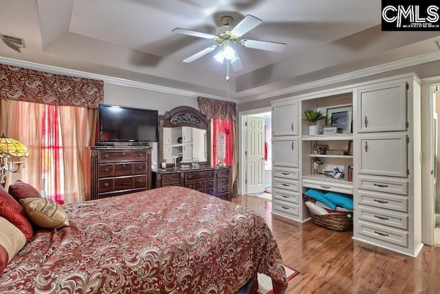 bedroom with crown molding, ceiling fan, wood-type flooring, and a raised ceiling