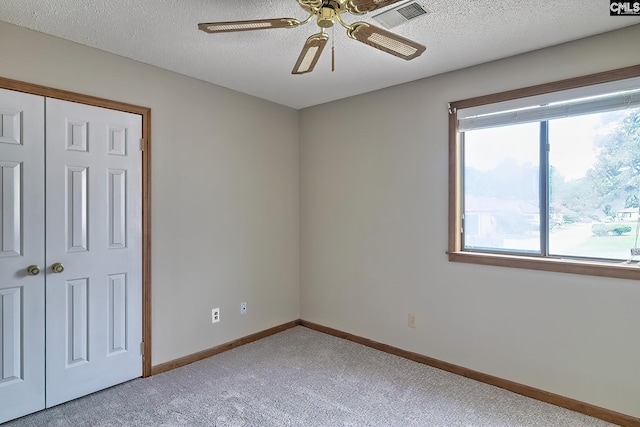 unfurnished bedroom featuring light carpet, ceiling fan, a closet, and a textured ceiling