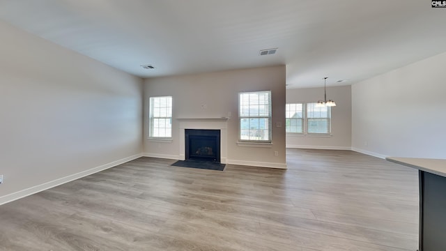 unfurnished living room with an inviting chandelier and light hardwood / wood-style flooring