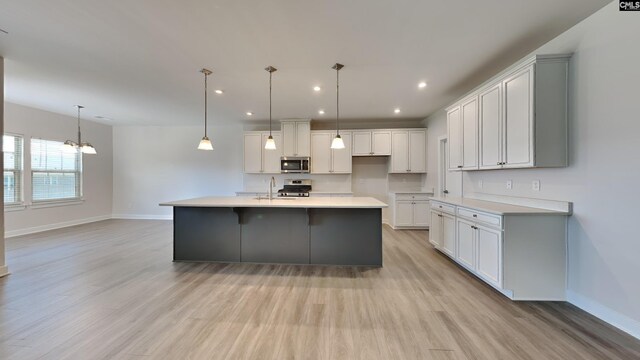 kitchen with light hardwood / wood-style flooring, appliances with stainless steel finishes, hanging light fixtures, and an island with sink