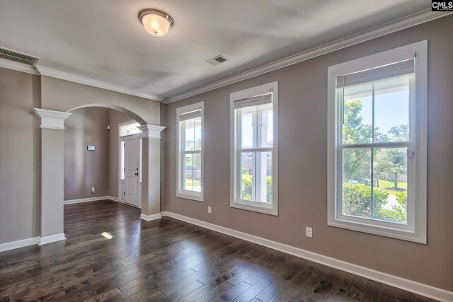 spare room with plenty of natural light, decorative columns, dark wood-type flooring, and ornamental molding