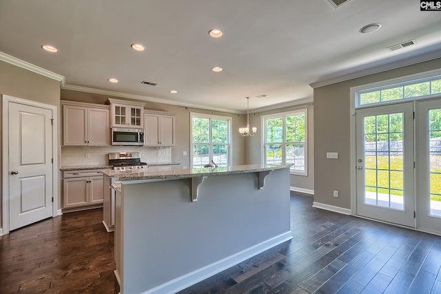 kitchen featuring decorative light fixtures, a kitchen island with sink, stove, a breakfast bar, and dark wood-type flooring