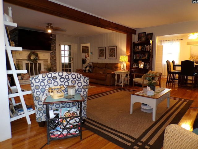 living room featuring wood-type flooring, beamed ceiling, a healthy amount of sunlight, and a brick fireplace