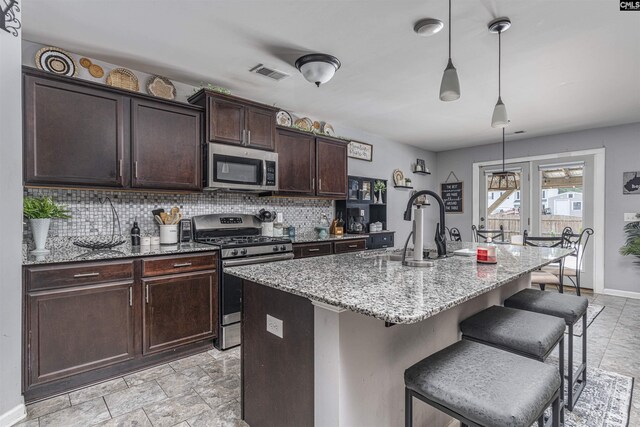 kitchen featuring pendant lighting, light stone countertops, a center island with sink, appliances with stainless steel finishes, and light tile patterned floors