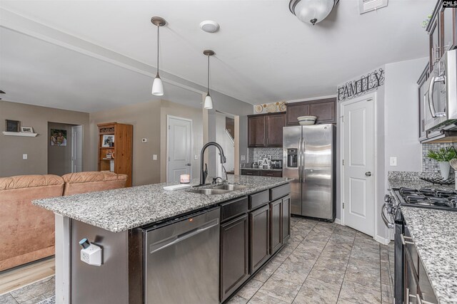 kitchen with hanging light fixtures, appliances with stainless steel finishes, light tile patterned floors, backsplash, and a kitchen island with sink