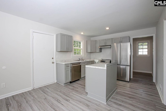 kitchen featuring a center island, stainless steel appliances, gray cabinets, light countertops, and light wood-style floors