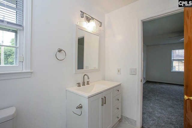 half bathroom with toilet, vanity, a wealth of natural light, and baseboards