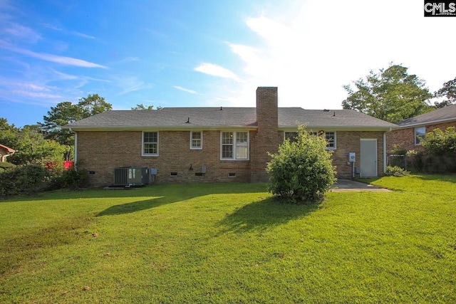 back of house with brick siding, crawl space, a chimney, and a lawn