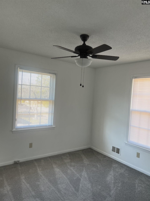 empty room featuring a textured ceiling, dark colored carpet, visible vents, and baseboards