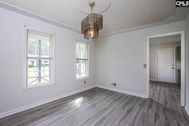 spare room with a textured ceiling, hardwood / wood-style flooring, and a notable chandelier