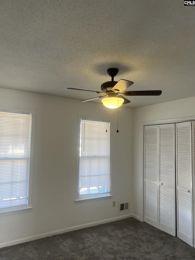 unfurnished bedroom featuring a textured ceiling, dark colored carpet, a closet, and visible vents