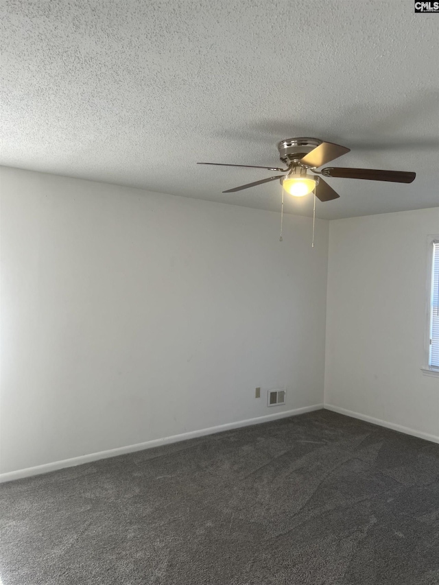 empty room featuring a textured ceiling, ceiling fan, visible vents, baseboards, and dark carpet