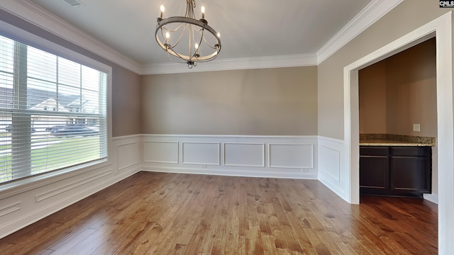 spare room with an inviting chandelier, ornamental molding, and light wood-type flooring