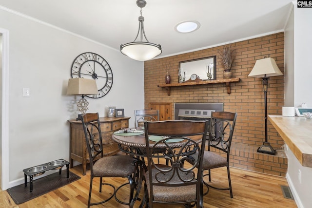 dining room featuring brick wall, crown molding, and light wood finished floors