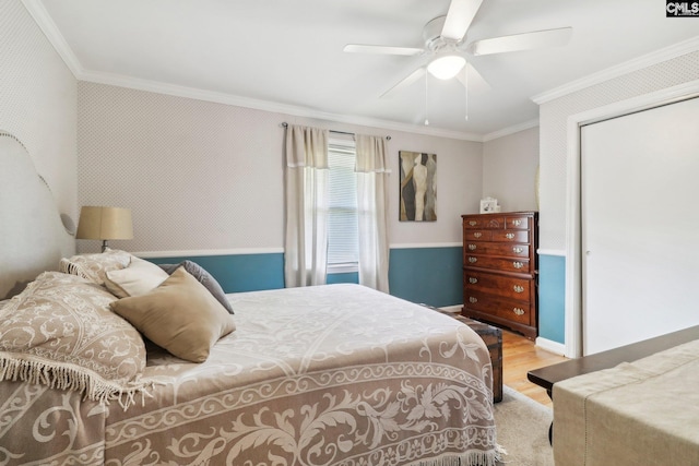 bedroom with wood finished floors, a ceiling fan, a closet, wallpapered walls, and crown molding