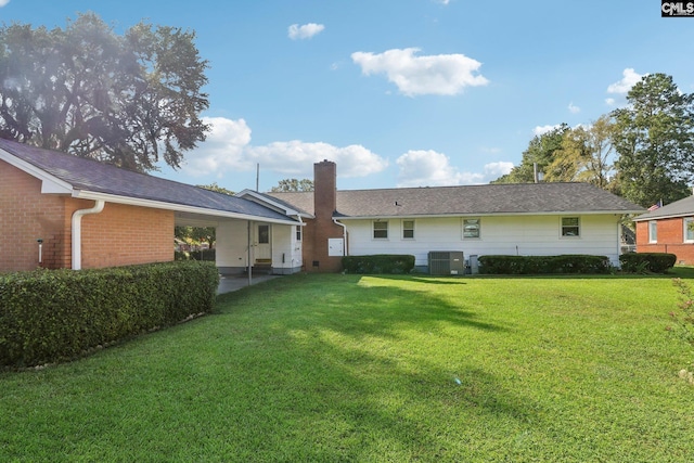 back of house featuring central AC unit, an attached carport, brick siding, a lawn, and a chimney