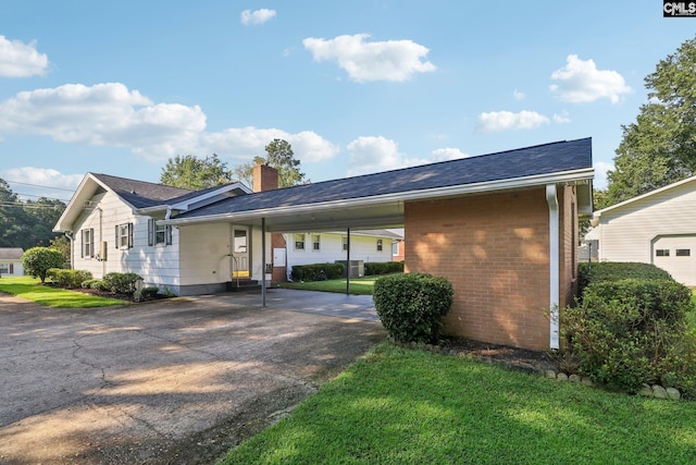 view of side of home featuring brick siding, a chimney, a lawn, a carport, and driveway