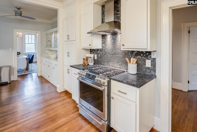 kitchen with light hardwood / wood-style floors, stainless steel range with gas cooktop, ceiling fan, white cabinets, and wall chimney range hood