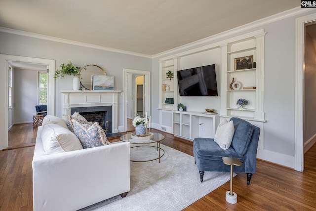 living room with a high end fireplace, wood-type flooring, built in shelves, and crown molding