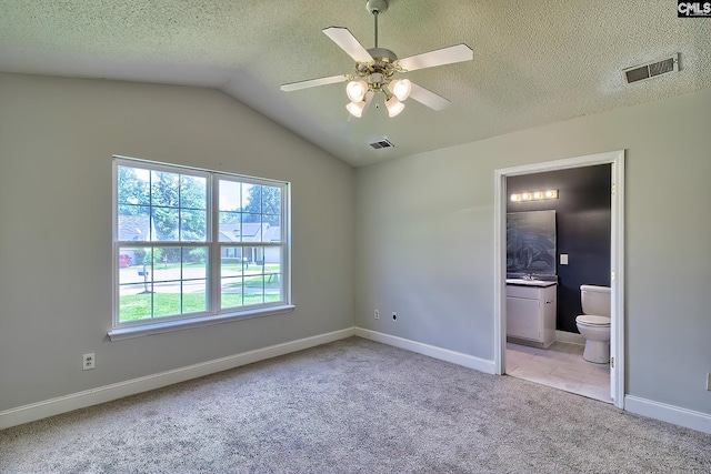 unfurnished bedroom with a textured ceiling, ceiling fan, light tile patterned floors, vaulted ceiling, and connected bathroom