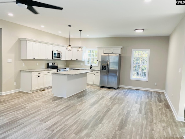 kitchen with a healthy amount of sunlight, a kitchen island, hanging light fixtures, and appliances with stainless steel finishes