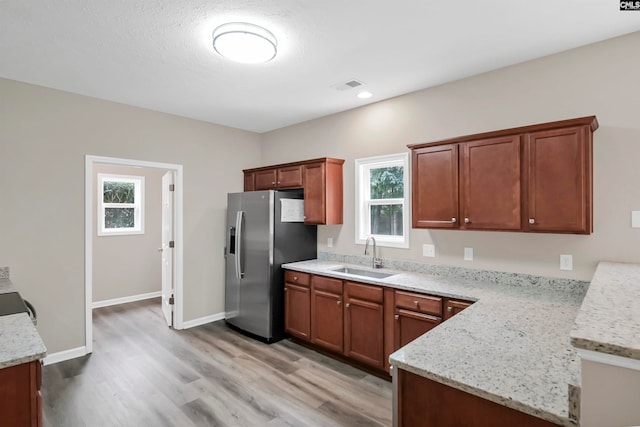 kitchen with stainless steel fridge, light wood-type flooring, sink, and light stone countertops