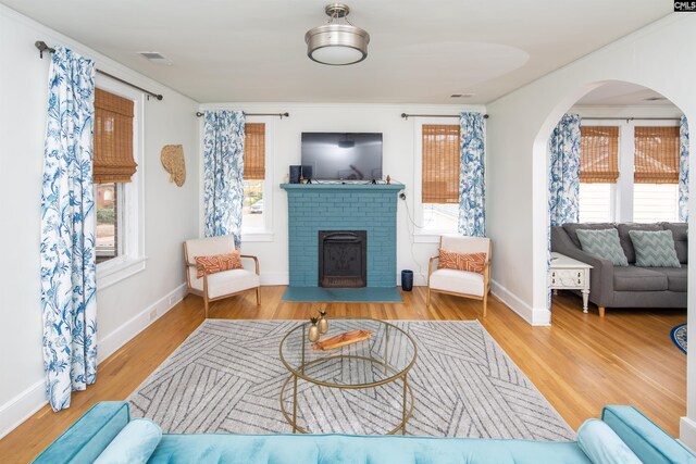 living room with light wood-type flooring, a brick fireplace, and crown molding