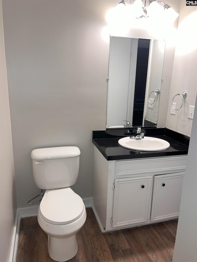 half bath featuring vanity, toilet, wood finished floors, and baseboards