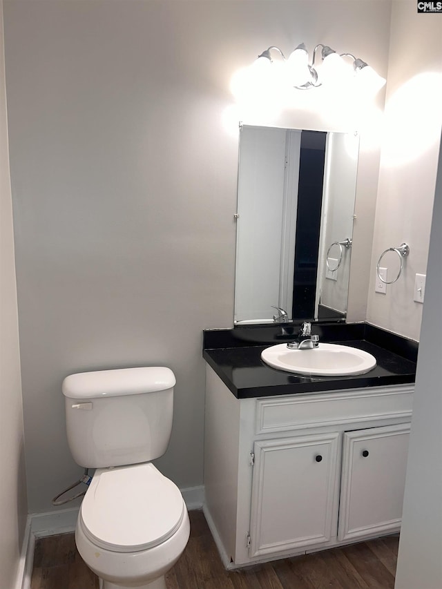 bathroom with vanity, toilet, wood finished floors, and baseboards