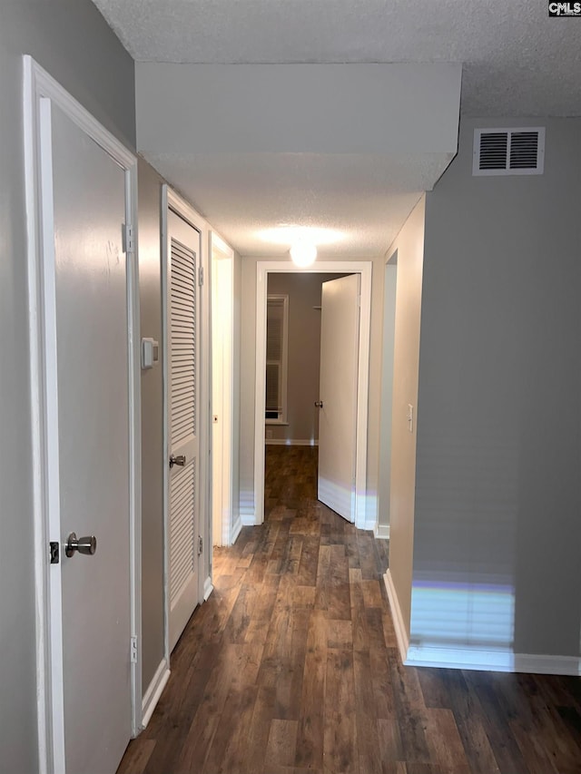 hall featuring visible vents, wood-type flooring, a textured ceiling, and baseboards