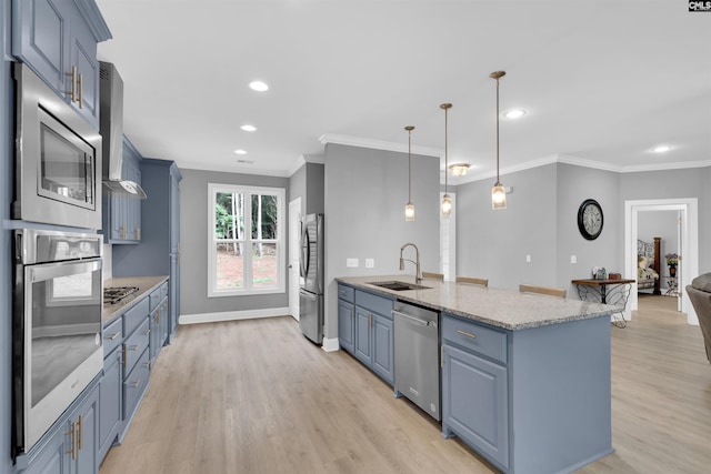 kitchen featuring appliances with stainless steel finishes, wall chimney range hood, pendant lighting, light hardwood / wood-style floors, and sink