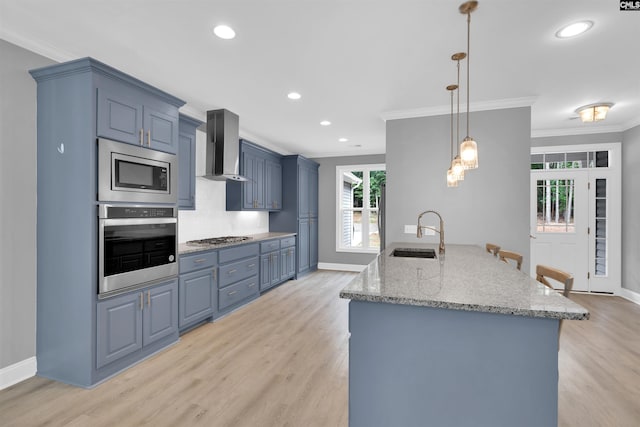 kitchen with appliances with stainless steel finishes, wall chimney range hood, sink, and light hardwood / wood-style floors