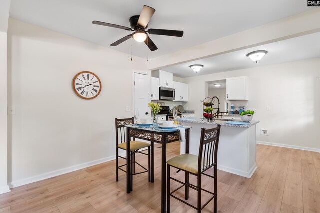 kitchen with light hardwood / wood-style floors, white cabinetry, sink, light stone counters, and ceiling fan