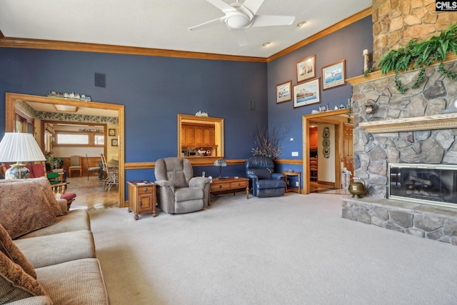 living area with ornamental molding, light carpet, a stone fireplace, and a ceiling fan