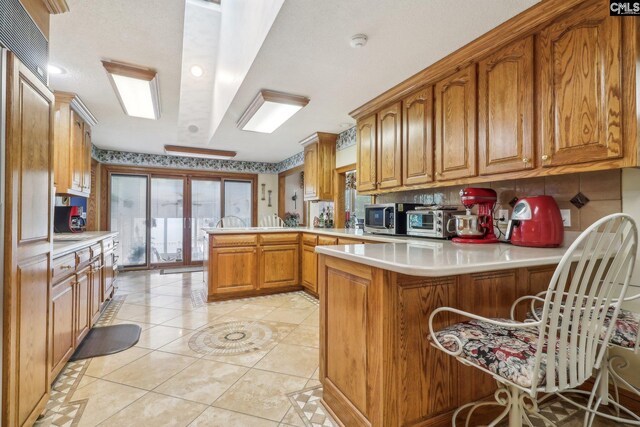 kitchen featuring brown cabinets, light countertops, stainless steel microwave, light tile patterned flooring, and a peninsula