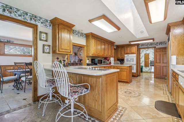 kitchen featuring stainless steel microwave, a peninsula, black electric cooktop, light countertops, and double oven