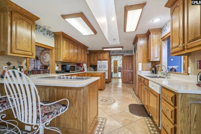 kitchen featuring brown cabinets, light countertops, stainless steel microwave, a sink, and a peninsula