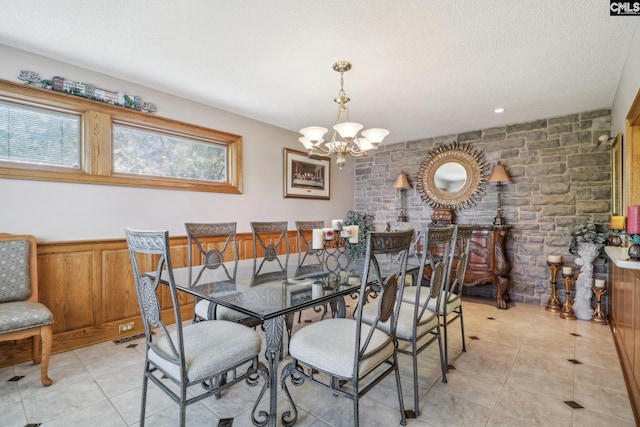 dining space with light tile patterned floors, wainscoting, a textured ceiling, and an inviting chandelier