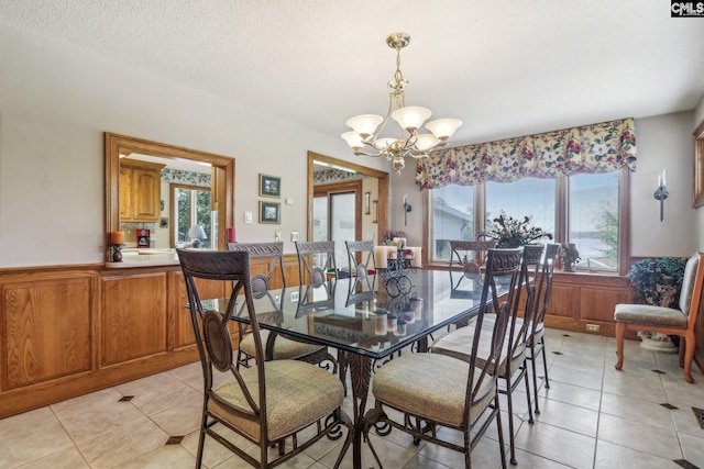 dining space with light tile patterned flooring, a chandelier, a textured ceiling, and wainscoting