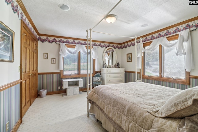 bedroom with ornamental molding, light colored carpet, a textured ceiling, and wainscoting