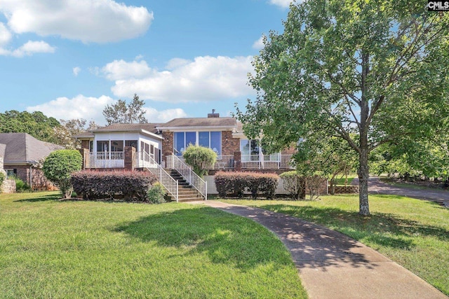 view of front facade featuring a sunroom, a chimney, stairway, a front lawn, and brick siding