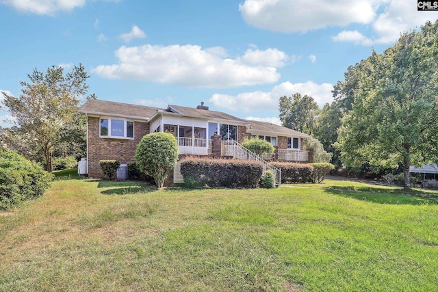 view of front of property featuring brick siding, a chimney, a front yard, and a sunroom