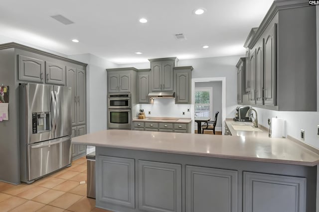 kitchen with gray cabinets, stainless steel appliances, a sink, visible vents, and a peninsula