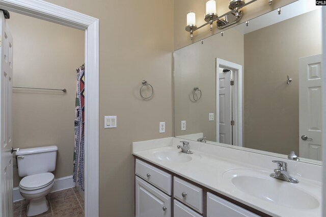 bathroom featuring baseboards, toilet, double vanity, and a sink