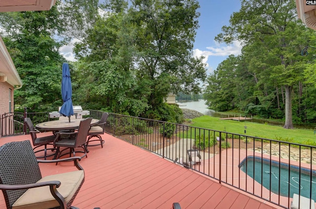 wooden deck with a yard, outdoor dining space, a water view, and a fenced in pool