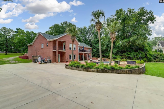 back of property featuring a wooden deck, a patio area, a yard, driveway, and brick siding