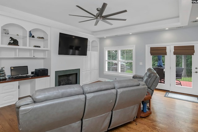 living room with ceiling fan, built in shelves, a raised ceiling, and hardwood / wood-style floors