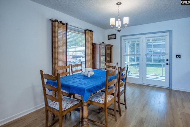 dining area featuring a textured ceiling, light wood finished floors, baseboards, and a notable chandelier