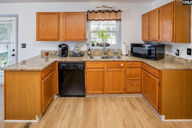 kitchen with light wood-style flooring, light stone counters, a peninsula, black appliances, and a sink